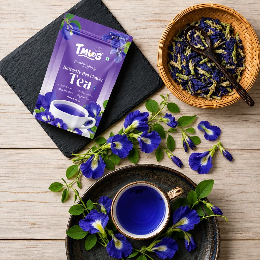 TMUG Butterfly Pea Flower Tea 100g pouch on a slate board beside a basket of dried blue flowers and a cup of blue tea